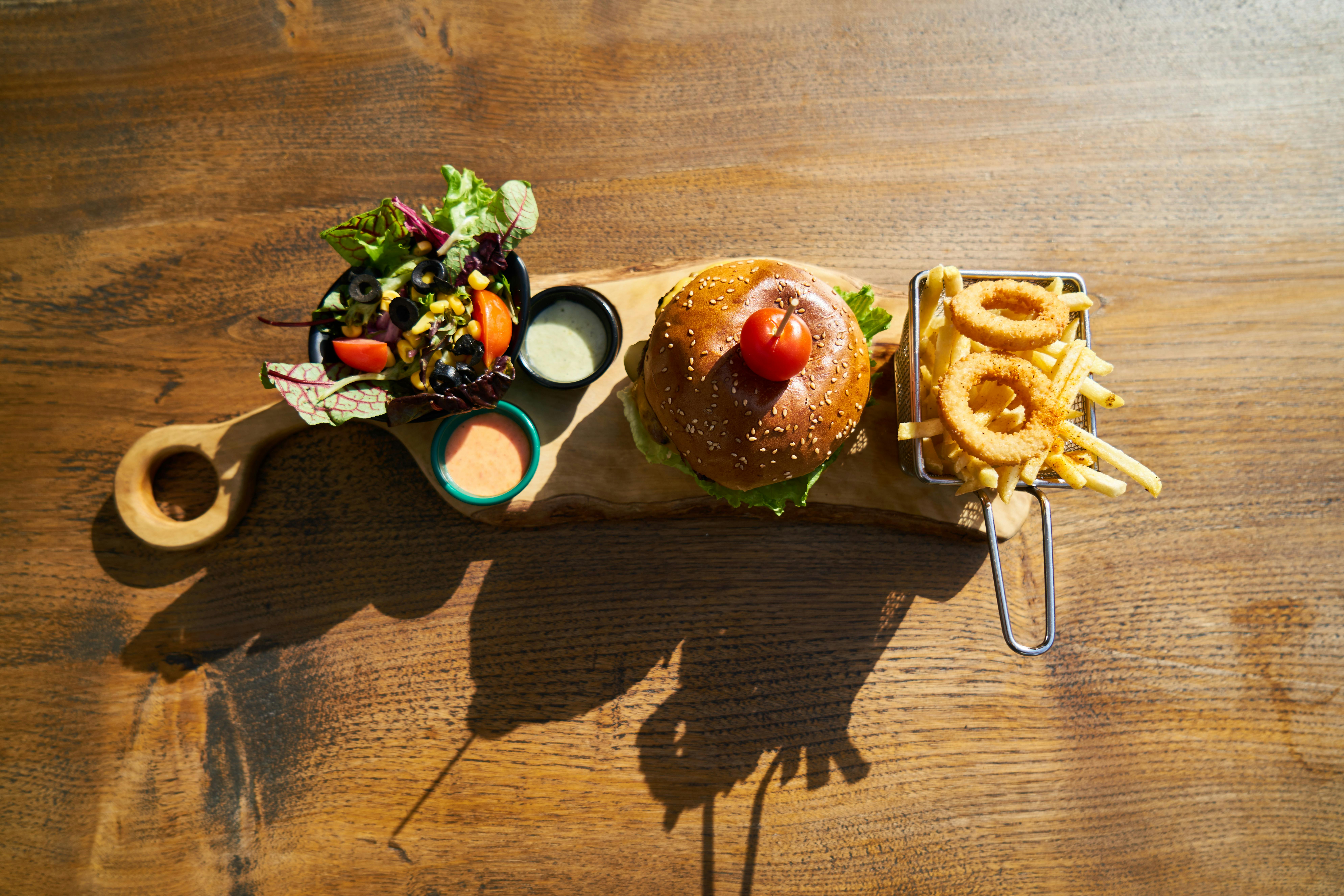 Delicious gourmet burger served with salad, fries, and onion rings on a rustic wooden board.